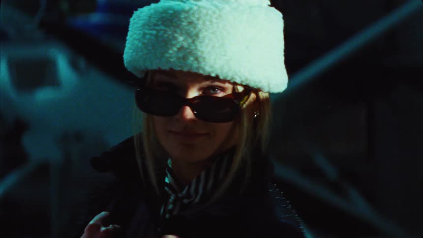 A stylish woman in a fuzzy hat and sunglasses gives a cool, mysterious look to the camera at night