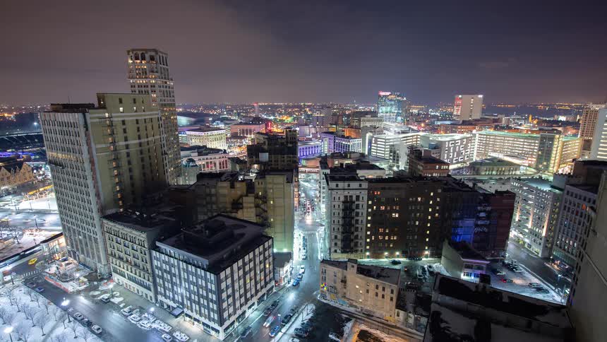 A high-angle time-lapse of downtown Detroit, Michigan, at night during winter, with snow-covered streets and bustling traffic