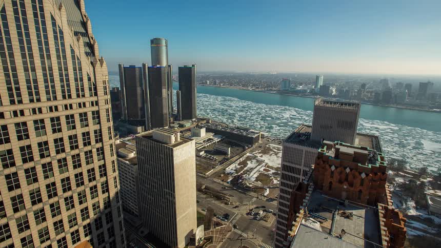 A sunny winter day timelapse shows traffic moving through downtown Detroit as ice floes drift down the frozen river