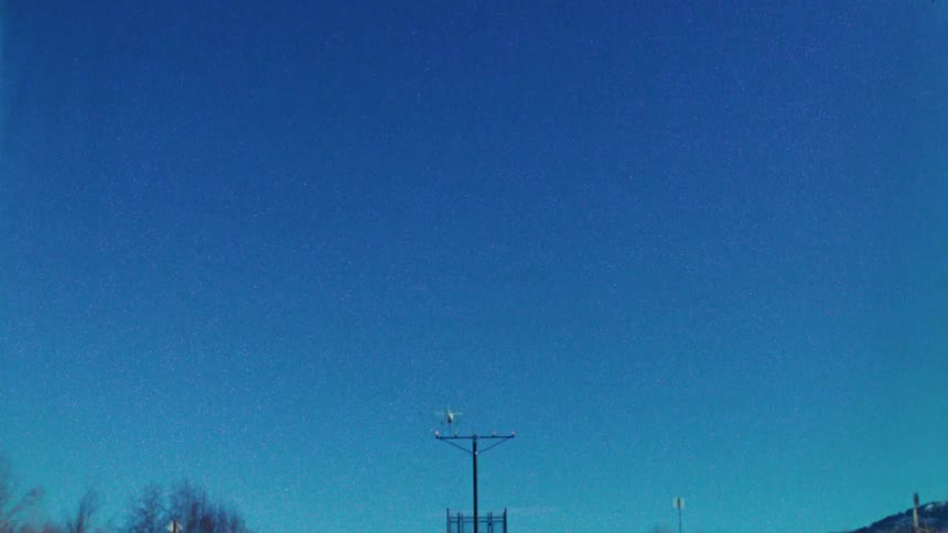 A small single-engine airplane flies directly overhead for a landing against a clear blue sky in this grainy, retro footage