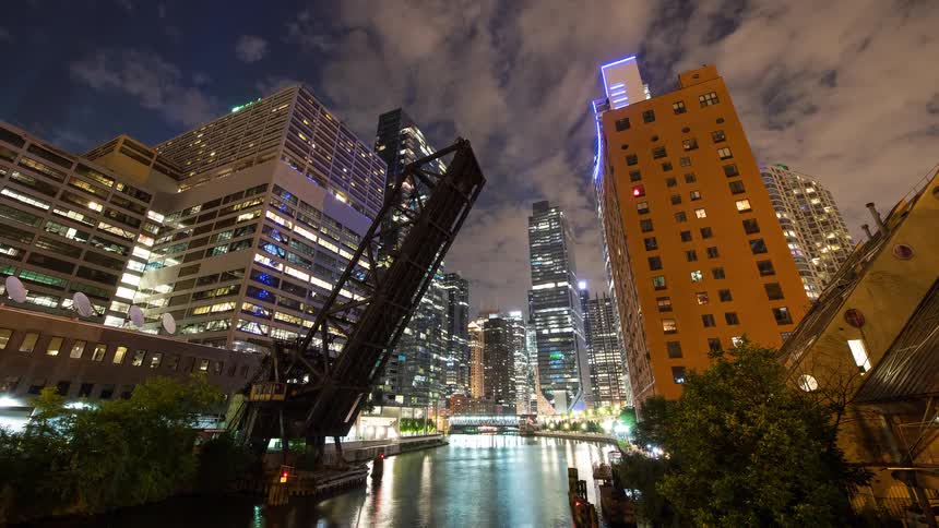 Dynamic night time-lapse of the Chicago River featuring a raised drawbridge, boat traffic, and the stunning illuminated city skyline