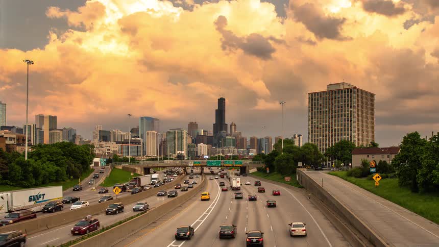 A stunning day-to-night time-lapse of traffic flowing on a highway into the Chicago skyline, transitioning through a colorful sunset to illuminated city lights
