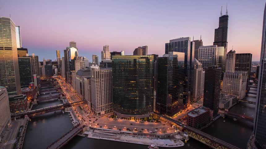 A beautiful day-to-night timelapse of the downtown Chicago skyline, featuring the busy river, bridges, and city traffic as the sun sets and the lights come on