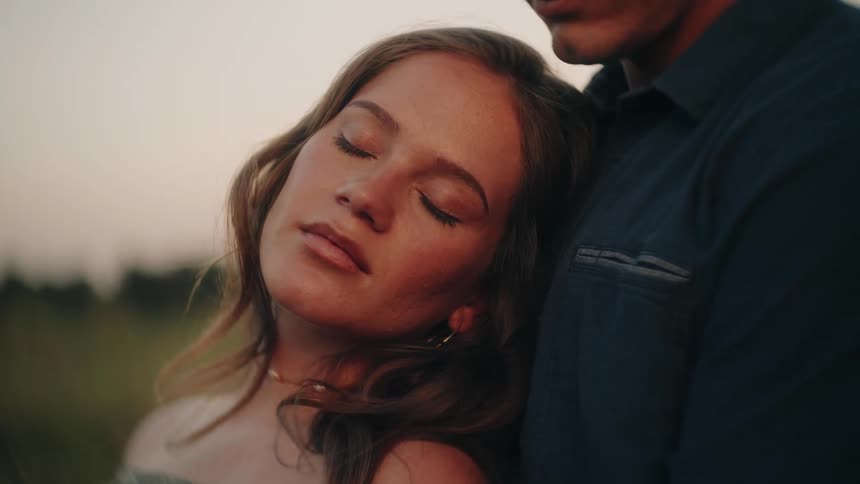 An intimate close-up of a serene woman with her eyes closed, resting her head on her partner's shoulder at sunset