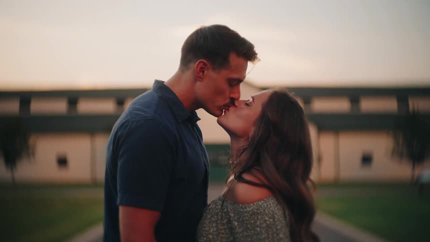 A couple in love shares an intimate slow-motion kiss outdoors at dusk in front of a rustic barn