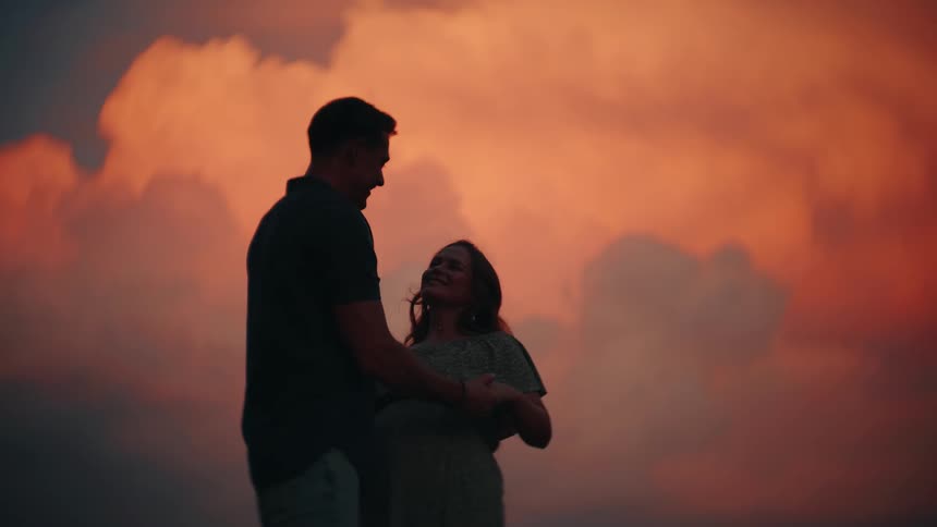 A romantic silhouette of an expecting couple dancing slowly and embracing against a beautiful sunset sky