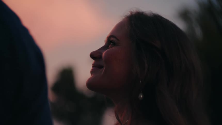 A slow-motion close-up of a woman smiling lovingly in profile against a warm sunset sky
