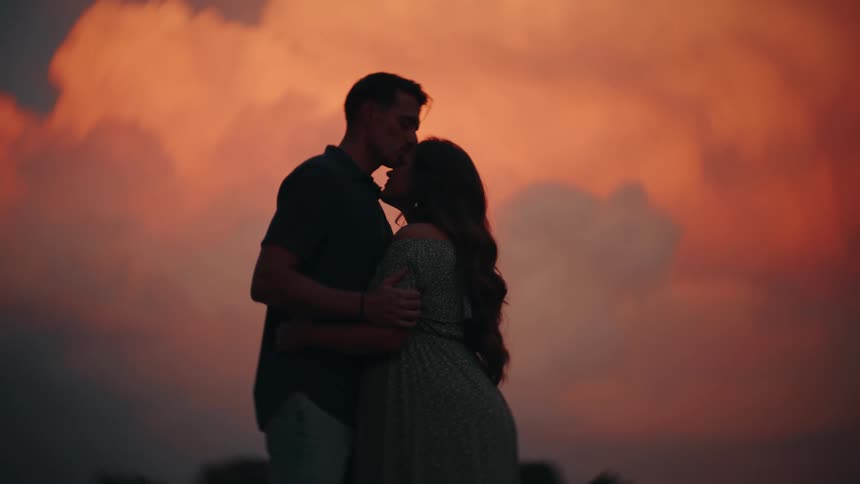 A silhouetted couple lovingly embraces and kisses against a beautiful and dramatic sunset sky