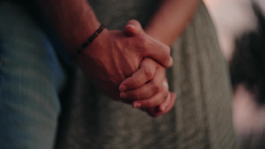An intimate close-up shot of a loving couple holding hands tightly together at sunset
