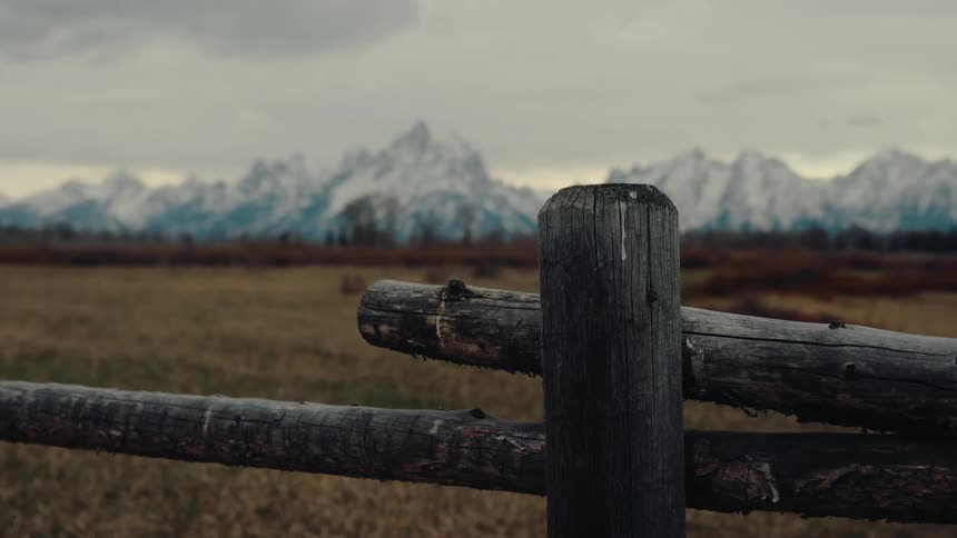 A cinematic close-up of a rustic wooden fence post with the magnificent snow-capped Grand Teton mountain range in the background