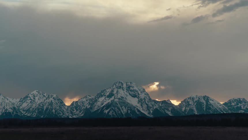 Stormy clouds roll across the sky above the magnificent snow-capped Grand Teton mountain range during a moody sunset
