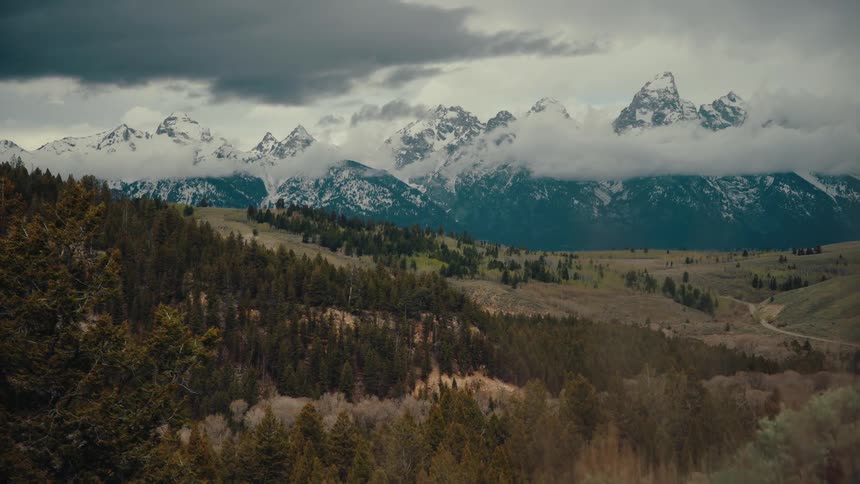 A majestic wide shot of the snow-capped Grand Teton mountain range under a dramatic, cloudy sky
