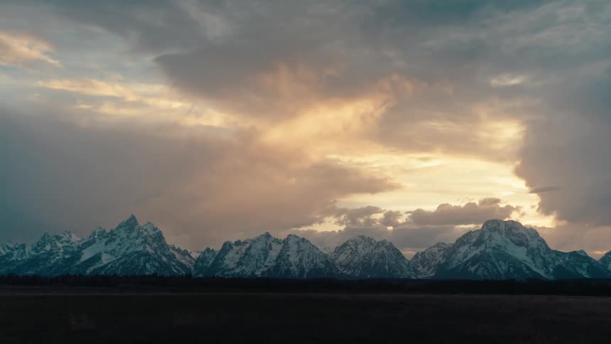 A dramatic timelapse of golden sunset clouds moving over the snow-capped Teton mountain range in Wyoming