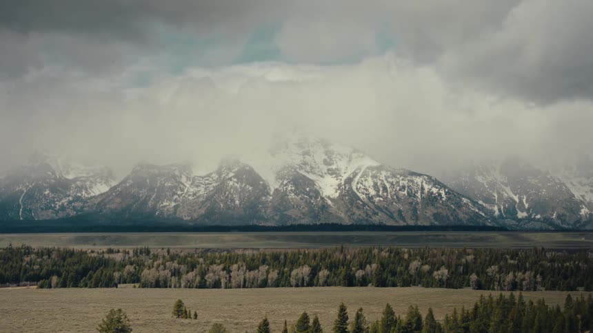 A dramatic time-lapse of clouds rolling over the snow-capped Grand Teton mountain range above a sprawling valley