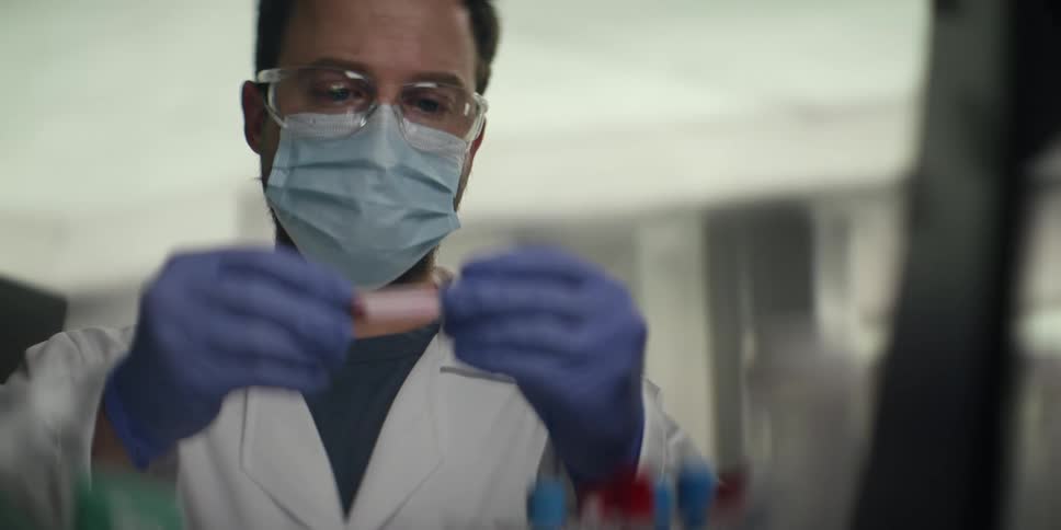 Focused male scientist in full protective gear meticulously examines a blood sample in a test tube in a modern laboratory