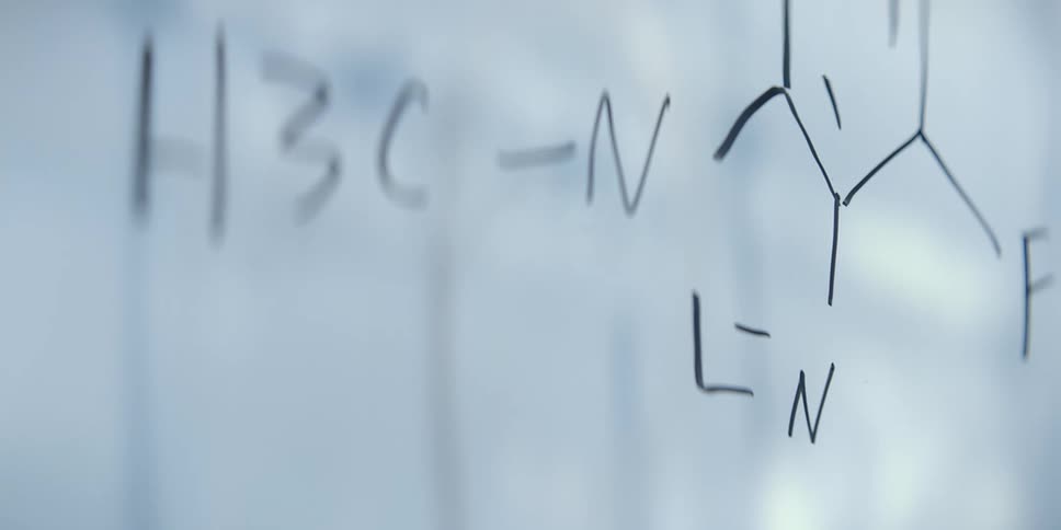 A close-up, shallow focus shot of a handwritten chemical formula on a white board