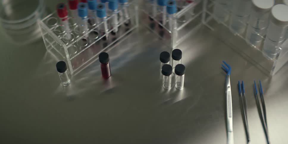 A scientist in a sterile lab picks up a syringe next to vials and test tubes containing blood samples