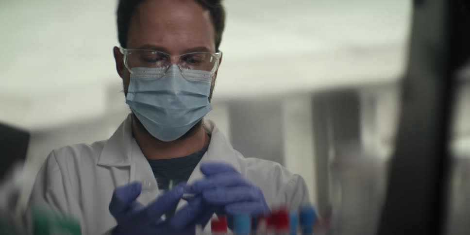A male scientist in a lab coat and protective gear carefully handles a petri dish while working in a laboratory