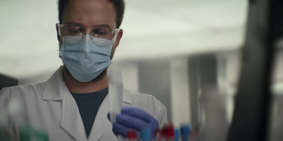 Close-up of a focused male scientist in full protective gear meticulously using a pipette to transfer liquid into a test tube in a laboratory