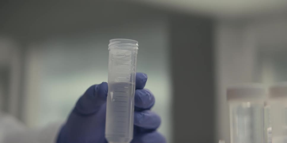 A scientist in a lab carefully uses a pipette to add a clear liquid to a test tube before sealing it with a cap