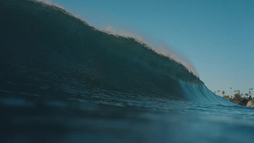 A stunning slow-motion shot from the water shows a perfect blue ocean wave curling into a barrel