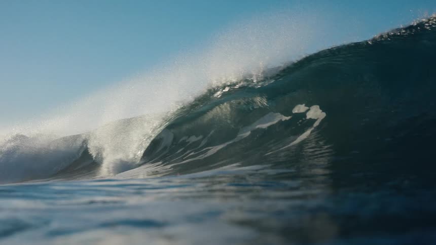 Epic slow-motion view from in the water as a perfect, sun-kissed wave curls and barrels towards the camera