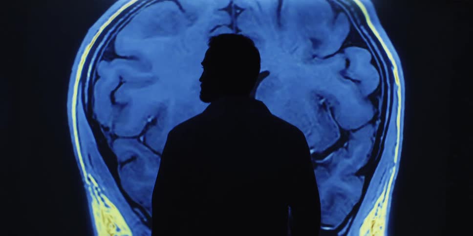 A silhouetted doctor observes a projected MRI scan of a human brain, analyzing the changing neural activity