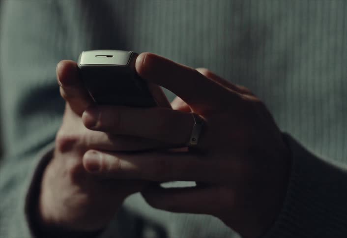 A close-up of a man's hands as he sends a text message on a vintage cell phone