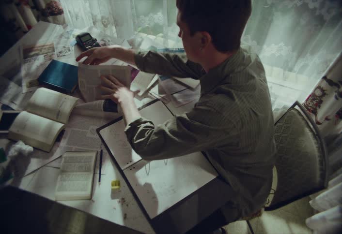 High-angle shot of a male student studying at a messy desk filled with books and papers, intensely researching for his project