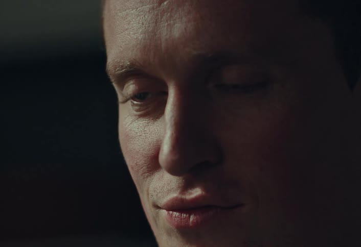 A man's face is shown in a moody close-up as he looks down in thought and then glances up