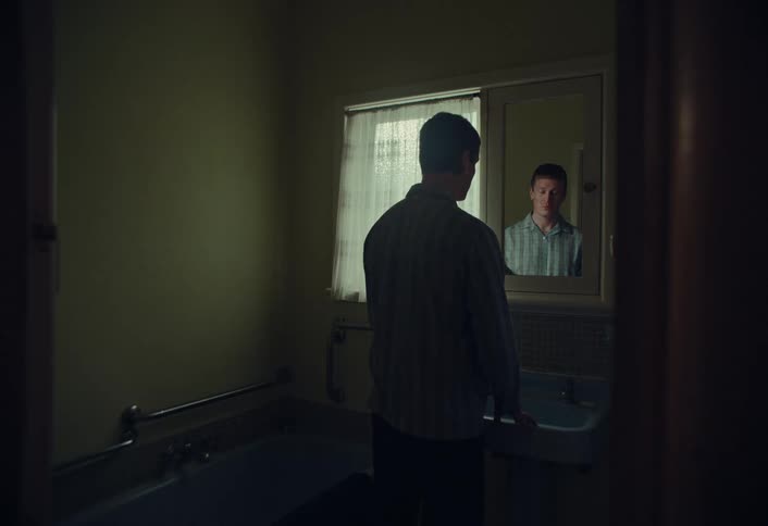 A cinemagraph shows a man's smiling reflection as he stands in a dimly lit, moody bathroom