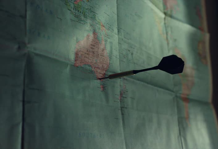 A dart marks Australia on a vintage world map, symbolizing a travel destination