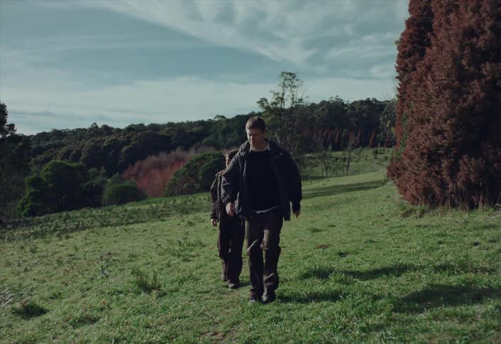 Cinematic slow motion of a young couple trekking up a grassy hill surrounded by nature