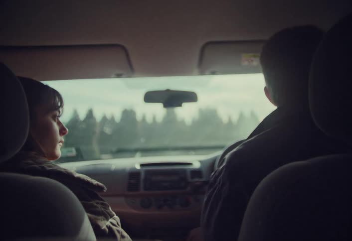 A couple shares an intimate moment holding hands while on a quiet road trip, seen from the back seat