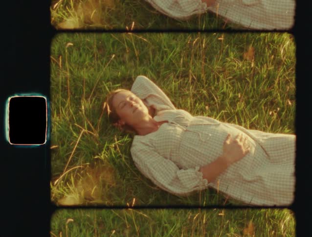 Vintage film footage shows a pregnant woman in a dress relaxing in a sunny meadow, holding her belly