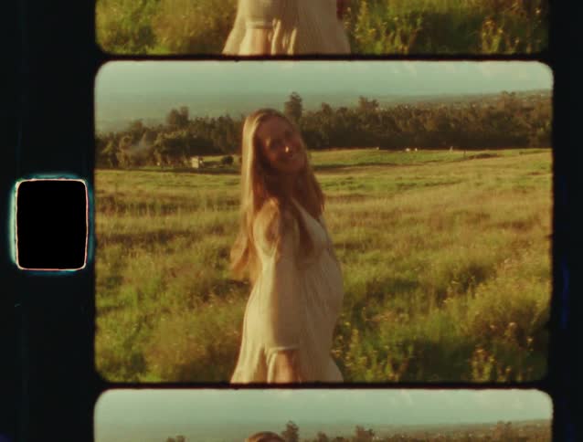 A beautiful pregnant woman dances and smiles in a golden sunlit field in this vintage 8mm style film