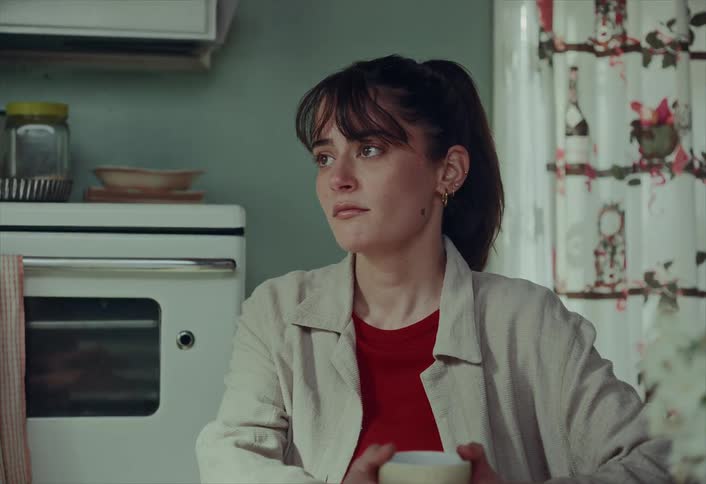 A pensive young woman sits thoughtfully at her kitchen table, her gaze lost in the distance