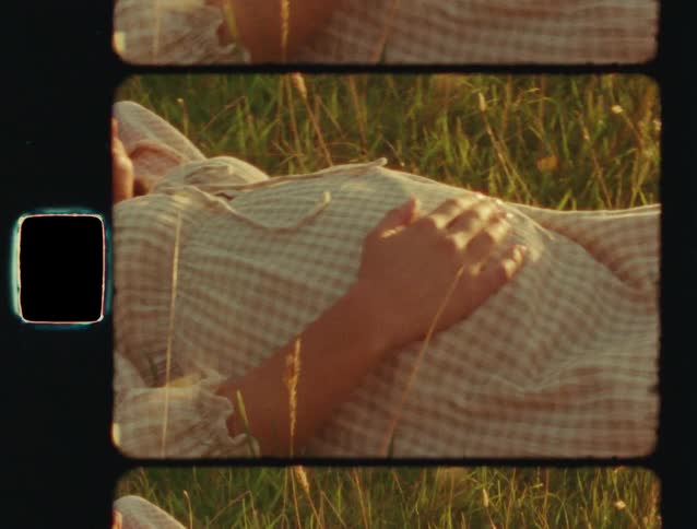 Vintage film shot of a pregnant woman in a gingham dress resting her hand on her belly while lying peacefully in a sun-drenched meadow