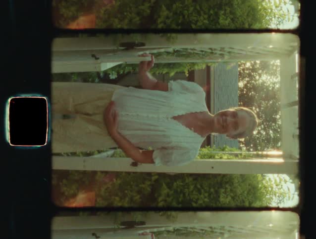 Vintage film shot of a pregnant woman smiling and holding her belly while standing in a garden at golden hour