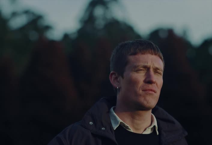 Close-up of a pensive young man looking off-camera, his face lit by the soft glow of twilight outdoors