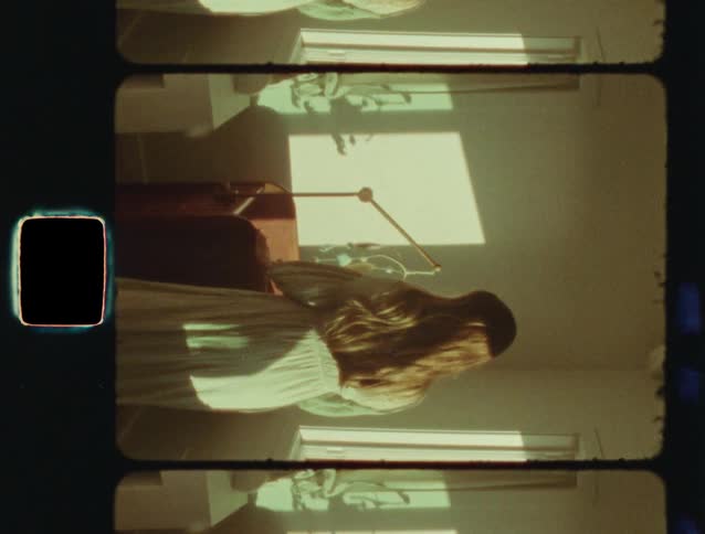 Vertical 8mm film captures a nostalgic scene of a woman in a vintage dress placing a flower on her sunlit desk