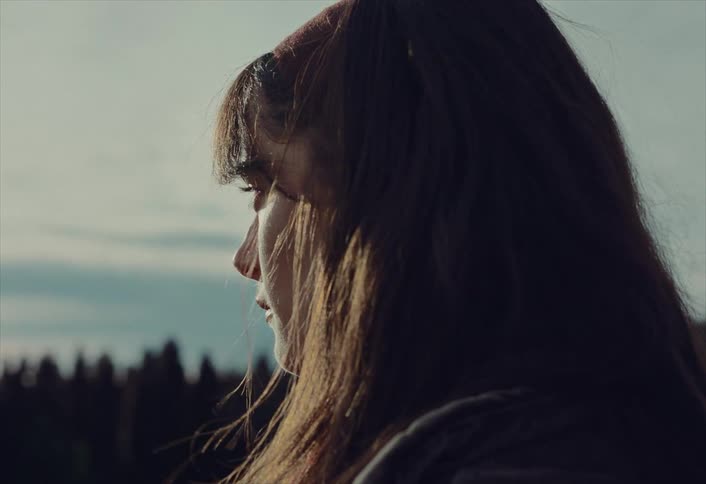 A melancholic close-up of a sad young woman looking over her shoulder with tears in her eyes before turning away in contemplation outdoors at sunset