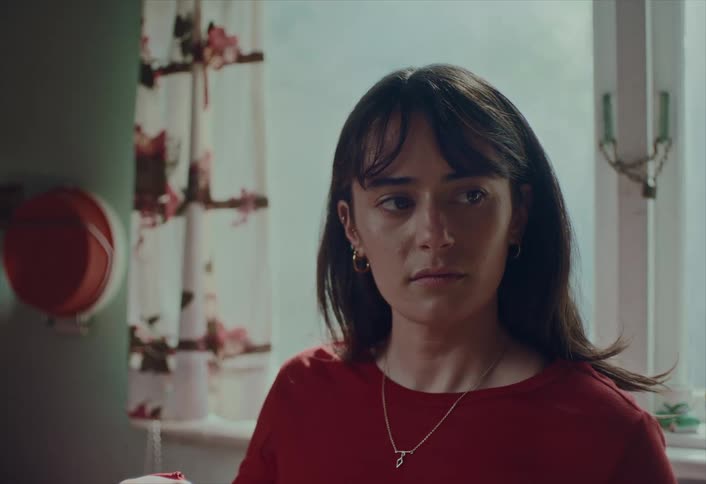 Close-up of a pensive young woman in a red shirt with a thoughtful and somber expression
