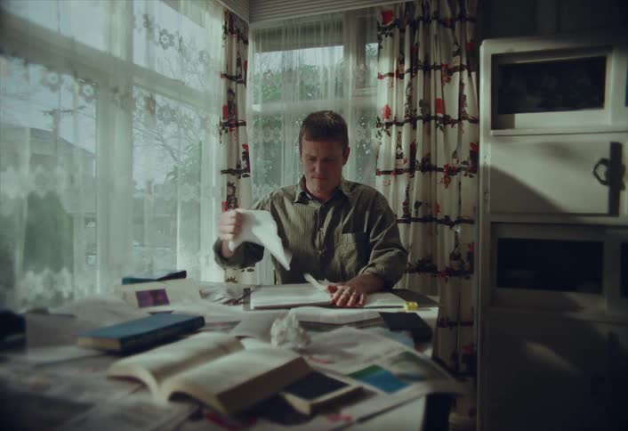 A frustrated writer or student crumples up a page from his notebook and throws it away after struggling with writer's block at his messy desk