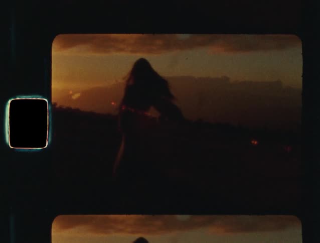 Vintage 8mm footage captures the silhouette of a woman dancing freely on a mountaintop during a golden sunset