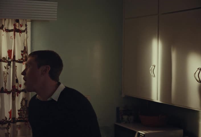 A lonely man drinks a glass of red wine and looks thoughtfully out the window in his dimly lit kitchen