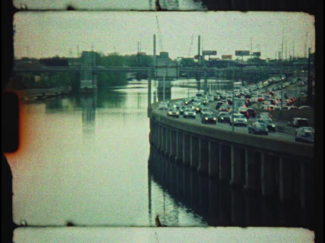 Authentic vintage 8mm film shows heavy rush hour traffic on a city highway adjacent to a river