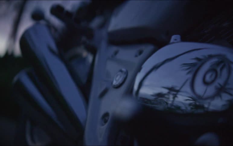 A moody close-up shot of a motorcycle's chrome engine and exhaust pipes reflecting the twilight sky