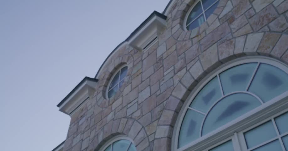 A slow-moving, low-angle shot captures the architectural details of a stone building with arched and circular windows against a clear sky