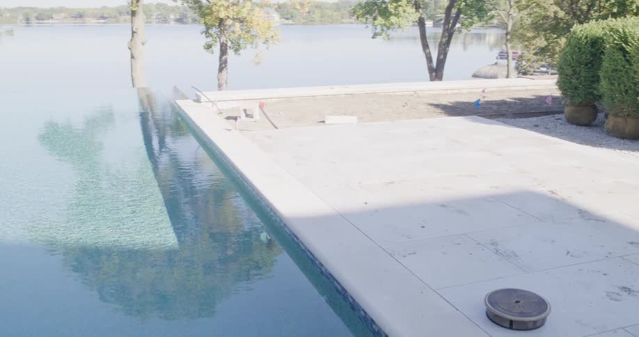 Slow pan reveals a modern infinity pool and patio being built on a luxury lakeside property